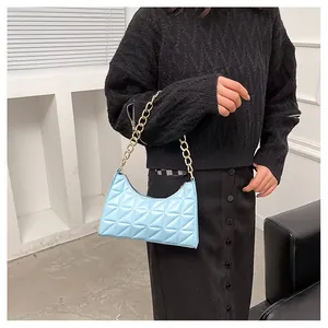 Detail of light blue quilted underarm bag with a bold gold chain strap and crescent shape