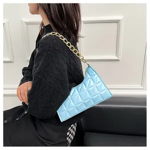 Detail view of light blue quilted underarm bag with chunky gold chain strap on shoulder