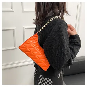 Detail of bright orange quilted baguette bag with chunky gold chain shoulder strap