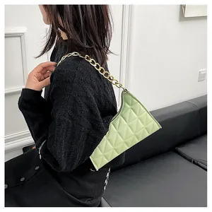 Detail of mint green quilted bag with chunky gold chain strap worn as a shoulder bag
