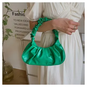 Close-up of bright green ruched cloud bag held by a model in a white dress