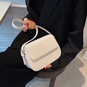 Detailed shot of white matte leather flap shoulder bag worn with a black blazer