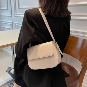 Detail view of a cream saddle bag with adjustable strap worn over a black blazer
