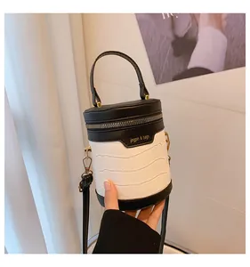 Detail einer schwarz-weißen Zylindertasche mit Krokodilprägung und goldenem Logo-Schriftzug