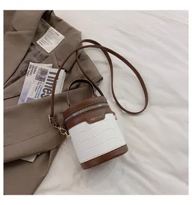 Detail der weißen Krokostruktur-Zylindertasche mit braunen Lederakzenten auf Stoff