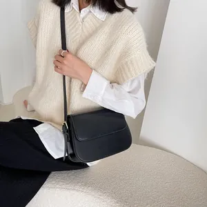 Detail of a minimalist black leather saddle bag with gold hardware and flap closure