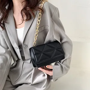 Fashionable black quilted shoulder bag with gold chain strap on grey blazer