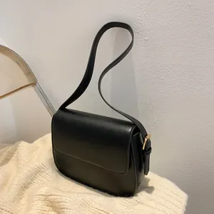 Detail of minimalist black faux leather shoulder bag with gold metal buckle and stitching