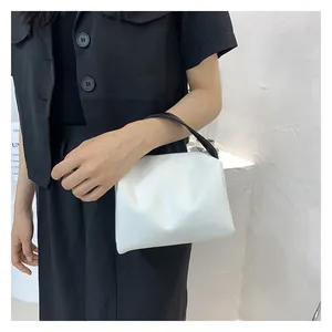 Detail of minimalist white leather handbag with contrast black handles and pleated texture