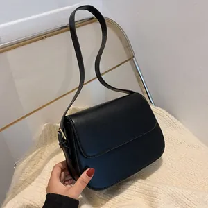 Detail view of black leather shoulder bag with glossy finish and gold metal buckle