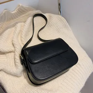 Close-up of black matte leather saddle bag with refined gold buckle on knit fabric