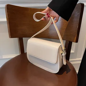 Detail of off-white minimalist saddle bag with gold metal buckle on a wooden surface