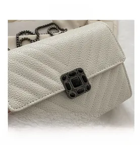 Detail of white caviar texture quilted handbag with vintage square metal lock and chain