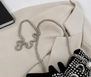 Detailed macro view of sparkling silver woven metal chain strap on black rhinestone bucket bag