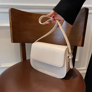 Close-up of a cream saddle shoulder bag with a metal buckle on a vintage wooden chair