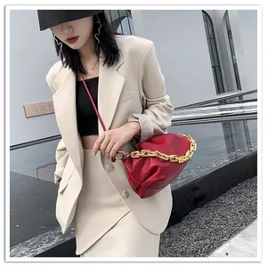 Detail of red ruched cloud bag featuring a bold gold chain handle and slim leather strap