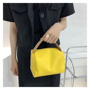 Detailed view of bright yellow handbag featuring brown handle on a black outfit