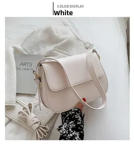 Detail view of a cream white saddle bag with golden metal buckles on a cozy background