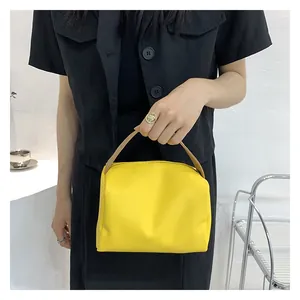 Detail of yellow box handbag with brown handles held by a model in black shirt