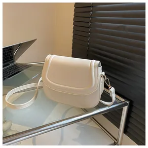 Detail view of cream saddle bag with matte leather finish and golden buckles in an office setting
