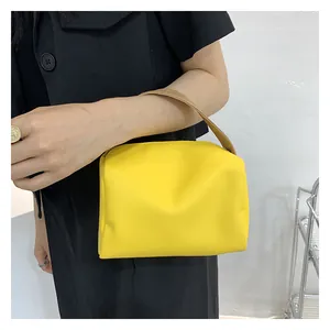 Detail view of yellow crossbody bag held by a model in a black dress against white wall