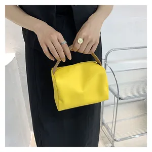 Detail of a bright yellow textured mini square bag with brown leather top handles