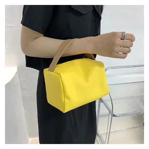 Detail of yellow rectangular handbag with beige handle held by a model in a minimal setting