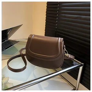 Detail of a brown leather saddle bag on a glass desk with clean stitching and gold metal hardware