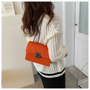 Detail shot of bright orange quilted crossbody bag with stylish chain strap and buckle