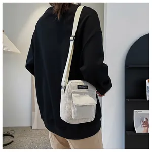 Detail of off-white corduroy crossbody bag showing adjustable strap and fabric brand label