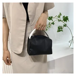 Minimalist black square handbag with contrast white handle held by model against white wall