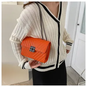 Detail of orange V-quilted crossbody bag with black buckle and metal chain strap