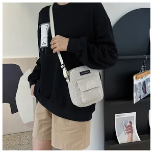 Detail of cream corduroy crossbody bag featuring a front flap pocket and woven label