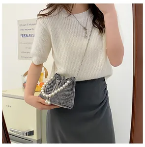 Detail of a sparkling black bucket bag with pearl handle and metal chain on a model