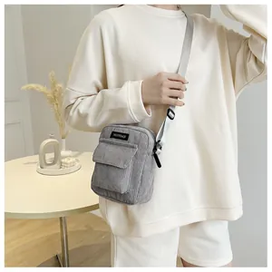 Detailed view of gray corduroy crossbody bag featuring a front pocket and adjustable strap