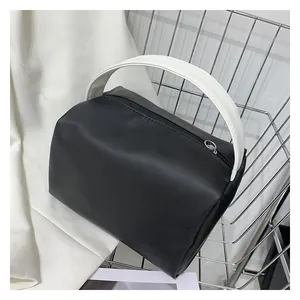 Detail of minimalist black handbag with contrasting white handle on a metal rack