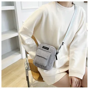Detail of grey corduroy crossbody bag featuring a front flap pocket and woven strap