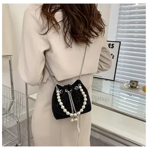 Detail of black rhinestone bucket bag with pearl handle worn by model in beige coat