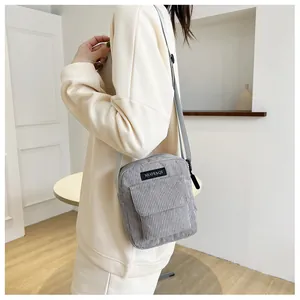 Detail of gray corduroy messenger bag featuring brand tag and adjustable strap