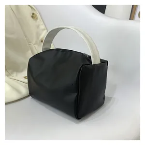 Close-up of a minimalist black square handbag featuring contrasting cream wide handles
