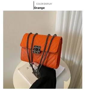 Close-up of orange V-quilted leather bag with black gem buckle and metal chain strap