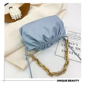 Close-up of light blue pleated cloud bag with chunky gold chain on a soft fabric
