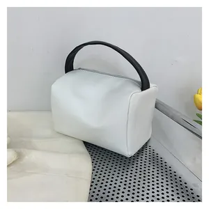 Detail of white leather crossbody bag featuring contrasting black round handle and zip