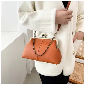 Close-up of orange litchi-grain leather shell bag with metal clip and gold chain detail