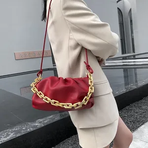 Red pleated cloud crossbody bag with gold chain strap carried by model in beige suit
