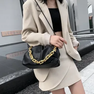 Chic black pleated cloud bag with chunky gold chain strap worn over a beige suit jacket