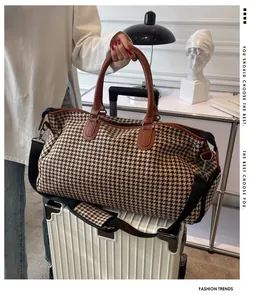 Dettaglio borsa da viaggio pied-de-poule con manici in pelle sopra una valigia rigida