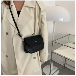 Detail of black leather crossbody bag with woven flap texture worn over beige coat