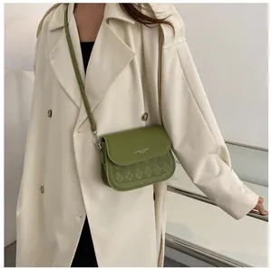 Detail of green saddle bag with diamond quilting and white graphic text on beige coat