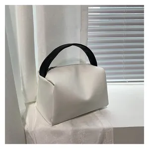 Detail of minimalist white leather handbag featuring contrasting black handles and sleek zipper
